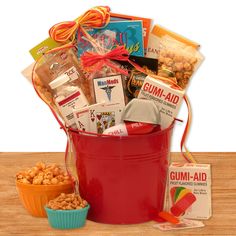 a red bucket filled with lots of different types of snacks and candys on top of a wooden table