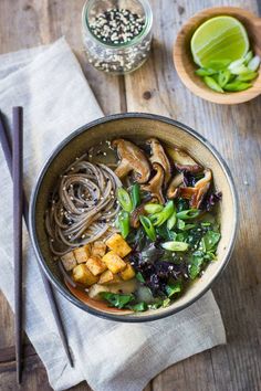 a bowl filled with noodles and vegetables on top of a wooden table next to chopsticks