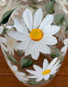 a glass vase with white and yellow flowers painted on the side, sitting on a wooden table