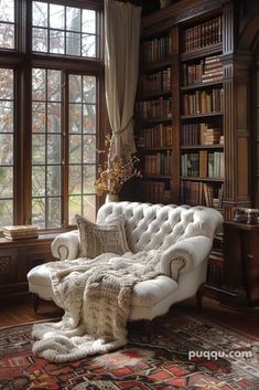 a white couch sitting in front of a window next to a book shelf filled with books