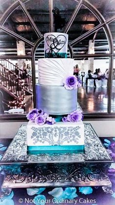 a three tiered cake with purple flowers on the top and bottom is sitting on a silver platter