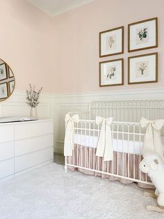 a baby's room with pink walls, white crib and pictures on the wall