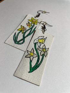 two white earrings with yellow and green flowers on them sitting on top of a table