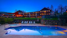 an outdoor swimming pool with chaise lounges and lights around it at night time