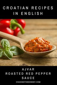 a wooden spoon filled with sauce next to red peppers and basil on top of a table