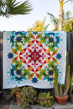 a colorful quilt hanging on a fence next to cacti and succulents