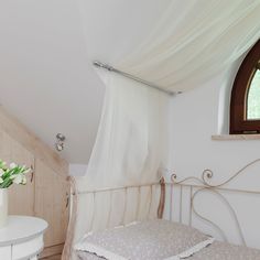 a white bed sitting under a window next to a table with a vase on it