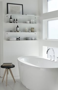 a white bath tub sitting in a bathroom next to a window with shelves above it