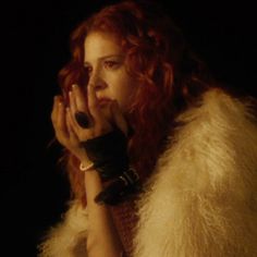 a woman with red hair is holding her hands to her face while wearing a fur coat