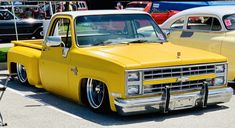 a yellow pickup truck parked in a parking lot next to other cars on display at a car show