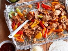 chicken fajita with peppers, onions and limes on aluminum foil next to tortillas