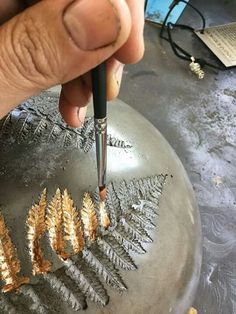 a person using a drill to paint gold leaves on a metal object with a black pen