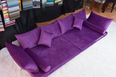 a large purple couch sitting on top of a white rug next to a pile of pillows