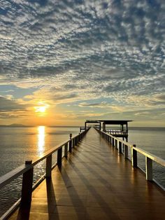 a long pier stretches out into the ocean as the sun sets over the water in the distance