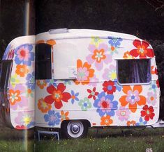 an old camper with flowers painted on it's side is parked in the grass