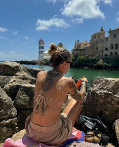 a woman sitting on top of a rock next to the ocean with a lighthouse in the background