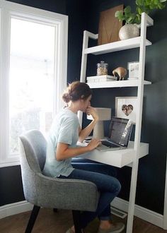 a woman sitting at a desk in front of a window with a laptop computer on it