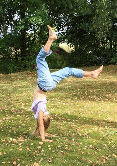 a young man doing a handstand in the grass with his legs spread out