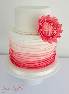 a three tiered cake with red and white icing on it, topped with a large flower