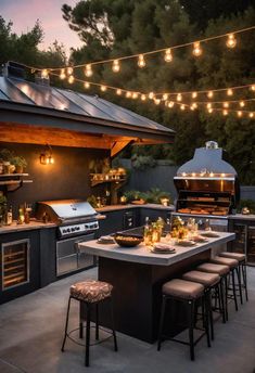 an outdoor kitchen is lit up with lights and string lights over the grill area, along with bar stools