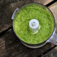 a food processor filled with green liquid on top of a wooden table