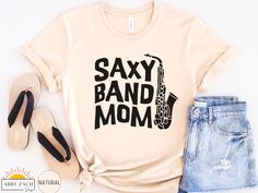 It's marching band season! This funny saxophone mom shirt will quickly become a wardrobe favorite of any marching band mom. We print on premium Bella and Canvas brand softstyle shirts for the ultimate comfort and softness. More marching band shirts available at my homepage https://www.etsy.com/shop/AbbyZachDesigns ----HOW OUR SHIRTS ARE MADE ----  * We use the process of DTG, which stands for direct to garment printing. We partner with a professional printer who applies ink directly into the shi Marching Band Parent, Marching Band Mom Shirts, Football And Band Mom Shirts Ideas, Band Mom Shirts Ideas Saxophone, Band Parent Shirts Ideas, Band Mom Shirts Ideas, School Band Shirts, Band Shirt Ideas, Funny Marching Band