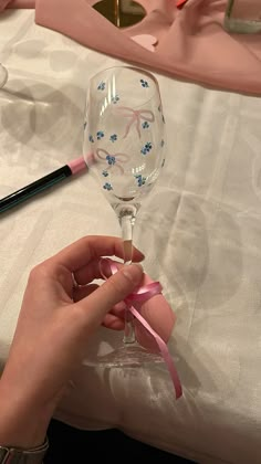 a person is holding a wine glass with pink ribbon on the table next to it