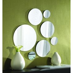 three white vases sitting on top of a table next to two round mirrors and a green wall