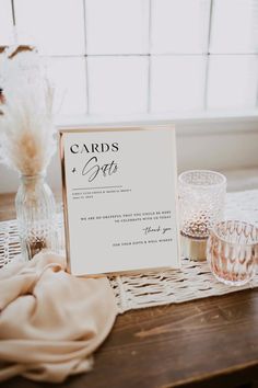 a table topped with glasses and cards next to a vase filled with dried flowers on top of a wooden table