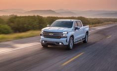 a silver truck driving down the road with mountains in the background and trees on either side