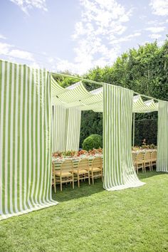 a green and white striped tent set up for an outdoor dining area with wooden table and chairs