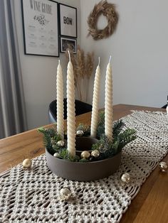 four white candles sitting on top of a wooden table next to a potted plant