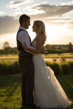 a bride and groom standing in the grass at sunset