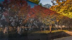 a large mural on the side of a building with trees in the background and people walking by