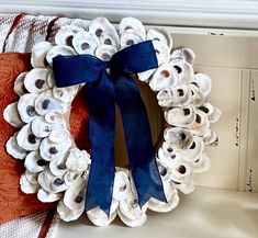 a wreath made out of seashells with a blue ribbon hanging from the front