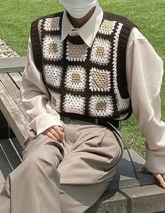 a man sitting on top of a wooden bench wearing a white hat and crocheted vest