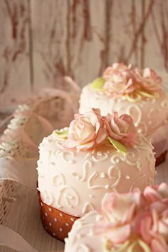 three decorated cakes sitting on top of a wooden table covered in pink and white frosting