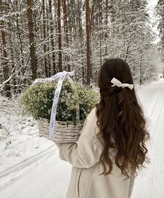 a woman walking down a snow covered road carrying a basket filled with flowers