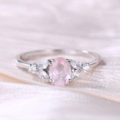 a pink ring with three pear shaped diamonds on it's side, sitting on top of a white cloth