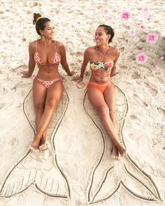 two women in bikinis sitting on the sand