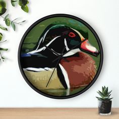 a clock with a painting of a duck on it's face next to a potted plant