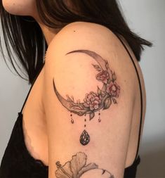 a woman's shoulder with a crescent and flowers tattoo on her left side arm