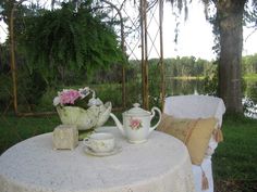 a white table topped with two cups and saucers next to a lush green field