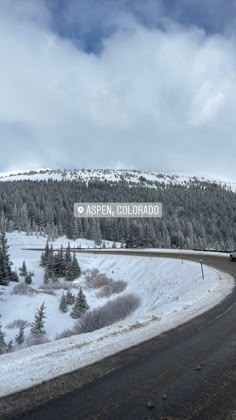 a road sign on the side of a snow covered mountain with trees in the background