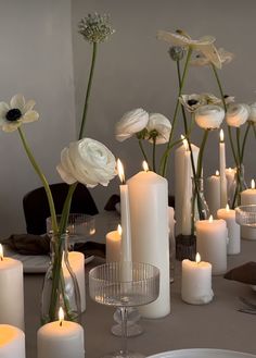 there are many white candles on the table with flowers in vases next to them