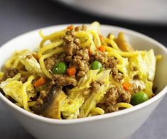 a white bowl filled with noodles and meat on top of a gray table next to two plates