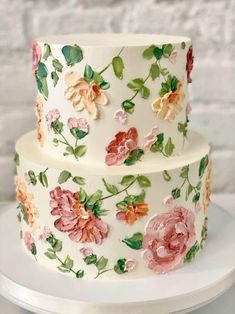 a three tiered cake decorated with flowers and leaves on a white plate next to a brick wall