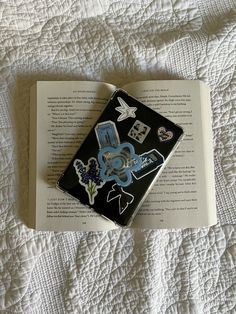 an open book laying on top of a bed covered in white sheets and decorative stickers