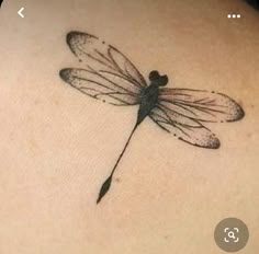 a small dragonfly tattoo on the back of a woman's shoulder