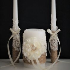 two white candles are decorated with flowers and burlocks